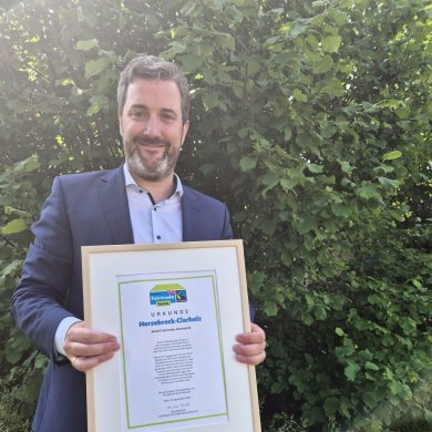 Bürgermeister Marco Diethelm mit Urkunde vor grünem Hintergrund