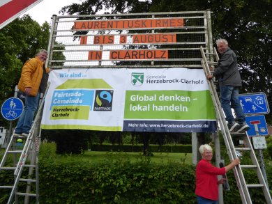 drei Menschen hängen ein Banner auf