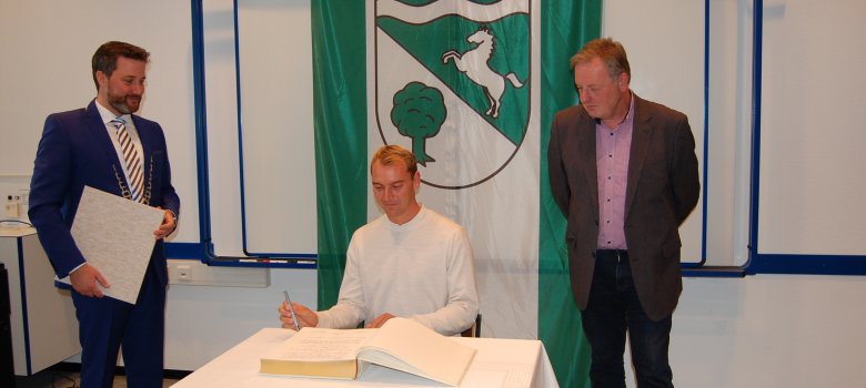 Cengiz Hartmann trägt sich ins Goldenen Buch der Gemeinde . Links von ihm Bürgermeister Marco Diethelm, rechts Hans-Hermann Strickmann.