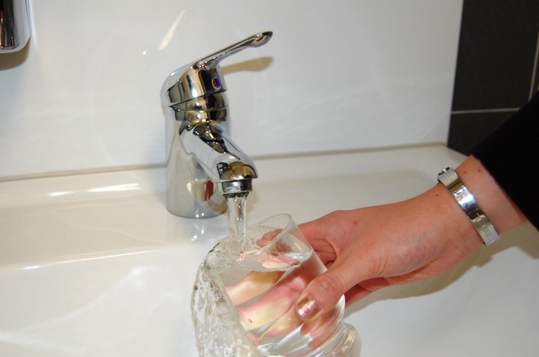 Hand und Glas mit Trinkwasser unter einem Wasserhahn am Waschbecken