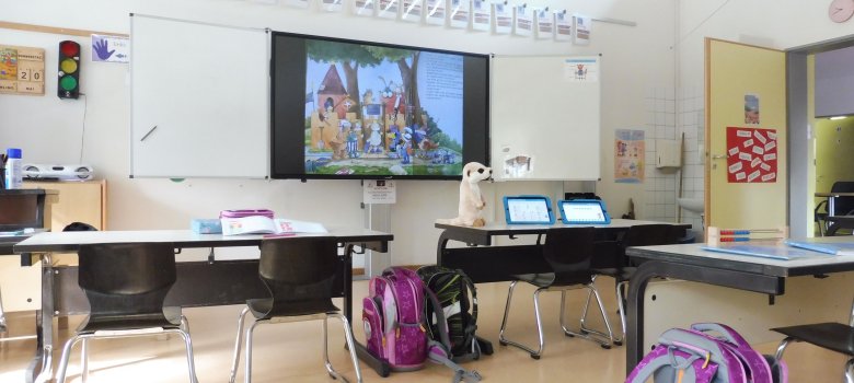 Das Bild zeigt Tische der Schülerinnen und Schüler vor einer interaktiven Tafel.