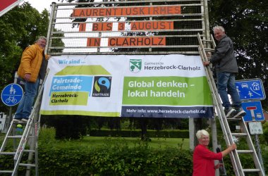 drei Menschen bei der Hängung des neuen Bannerss